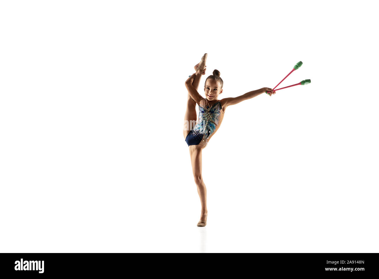 Petite fille souple isolé sur fond blanc studio. Peu de modèle féminin comme un artiste en gymnastique rythmique justaucorps lumineux. La grâce dans le mouvement, l'action et le sport. Faire des exercices avec les massues. Banque D'Images