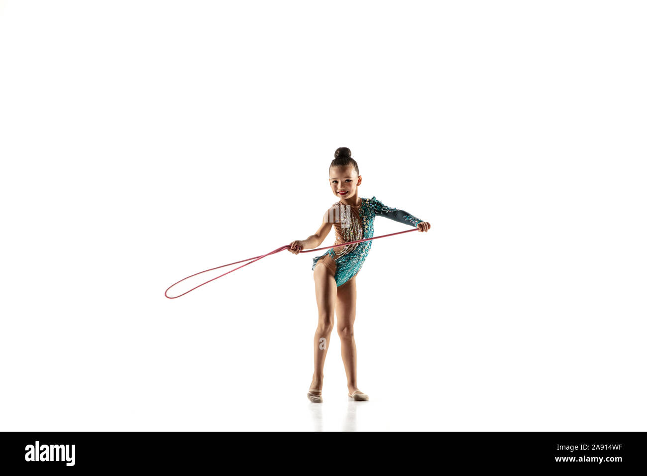 Petite fille souple isolé sur fond blanc studio. Peu de modèle féminin comme un artiste en gymnastique rythmique justaucorps lumineux. La grâce dans le mouvement, l'action et le sport. Faire des exercices avec la corde. Banque D'Images