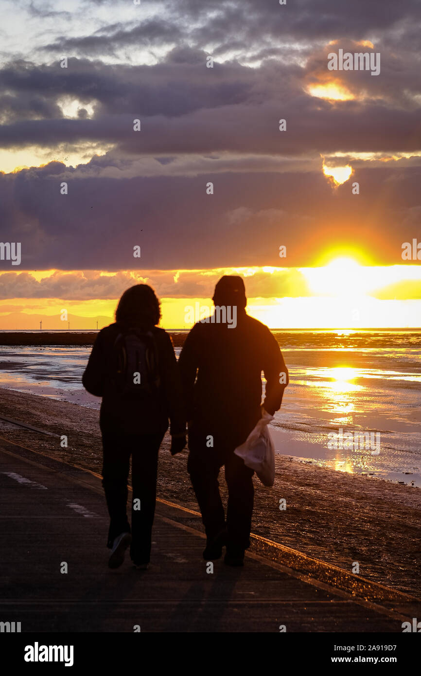 Un couple regardant le coucher de soleil sur la côte à Southport, dans le Nord-Ouest de l'Angleterre. Banque D'Images