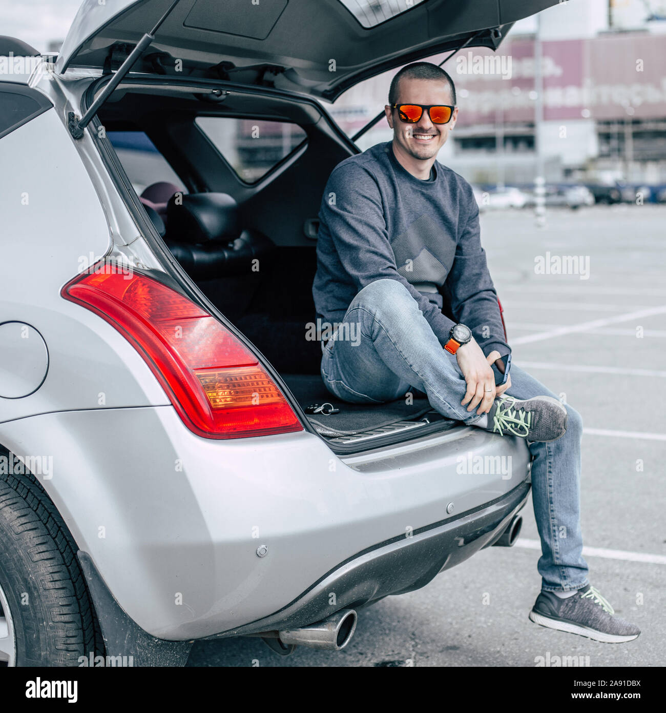 Des profils smiling man in sunglasses assis dans le coffre de sa voiture Banque D'Images