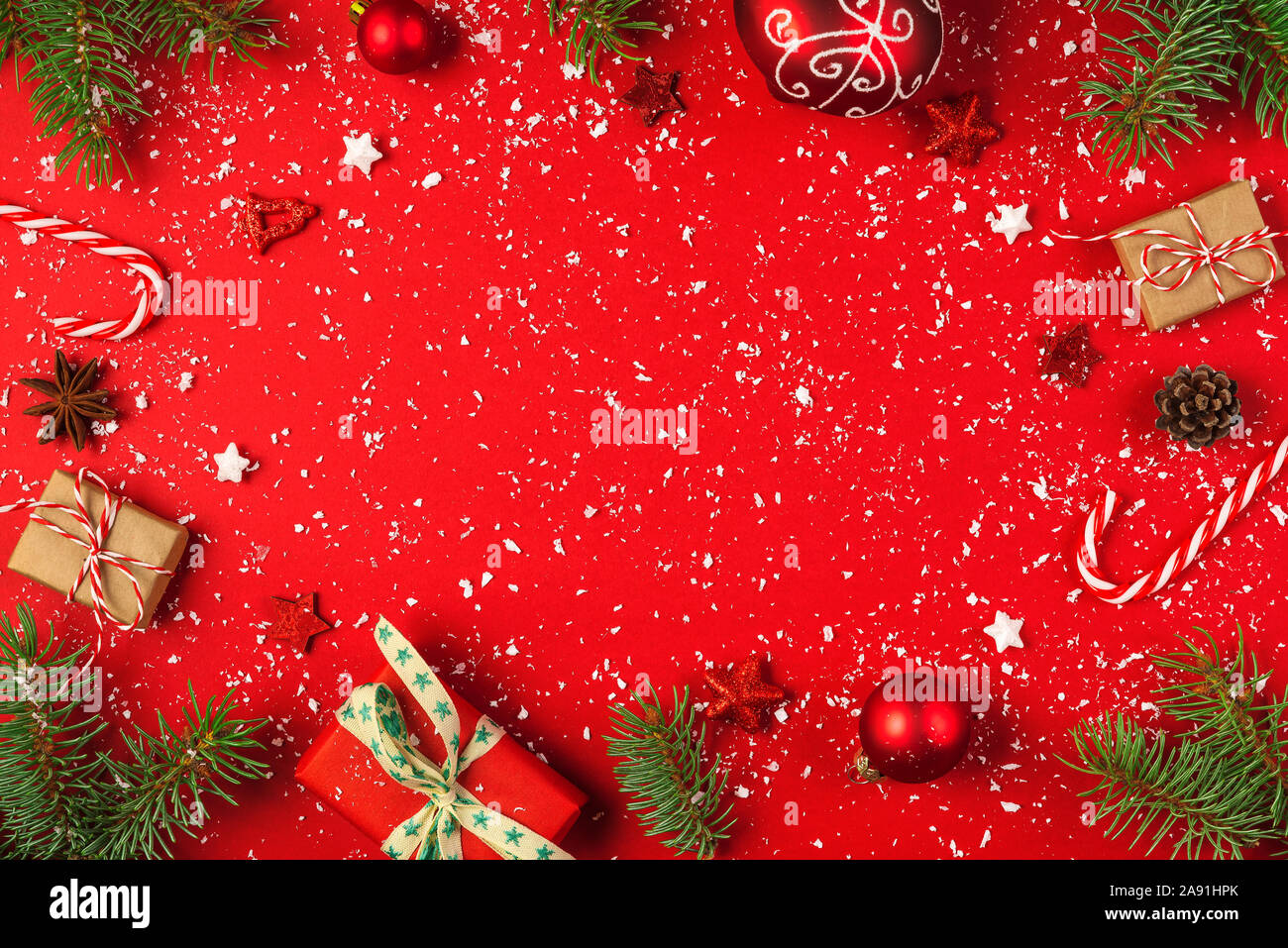 Cadre de noël faites de branches de sapin, des boîtes-cadeaux, des décorations de noël rouges et des bonbons sur fond rouge avec la neige. Noël ou bonne année concept. Banque D'Images