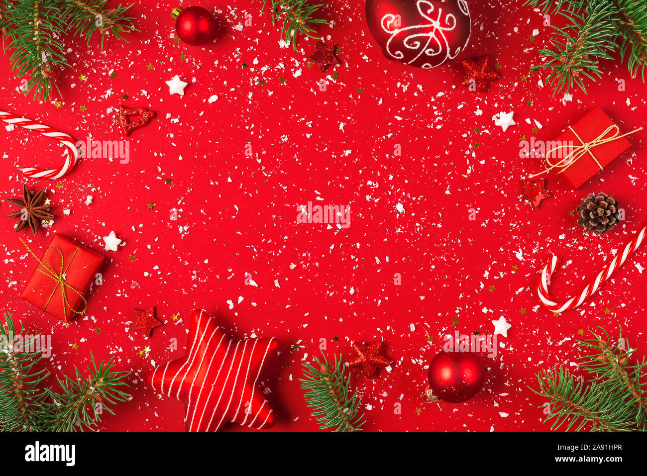 Noël ou bonne année la composition. Cadre fait de branches de sapin, des pommes de pin et des décorations de Noël sur fond rouge couverte de neige. Télévision. Banque D'Images