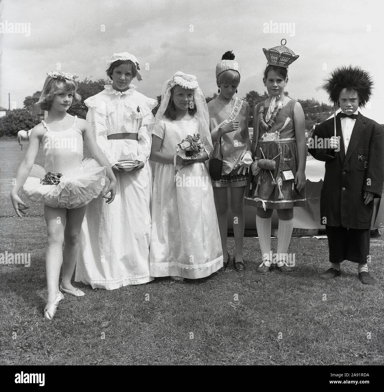 1967, historique, les enfants s'alignent dans leurs costumes pour la fantaisie robe de soirée à Speen fete, Angleterre, Royaume-Uni. Nous avons une variété de costumes en spectacle, y compris une danseuse de ballet, une mariée et une Miss Ascot. La jeune fille portant des brins de coton sur sa robe et un chapeau de paille est amusant mais pas sûr qui le jeune garçon sur la droite est censé être, mais aiment les dents!. Banque D'Images