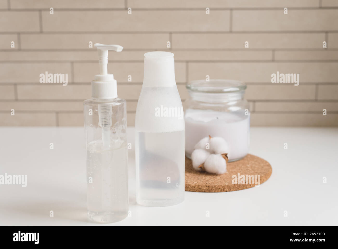 Accueil Soins de la peau, l'eau micellaire, crème et une bougie avec un coton fleur sur la table de chevet. Corps blanc et les cosmétiques de soins de la peau dans un moderne blanc ba Banque D'Images