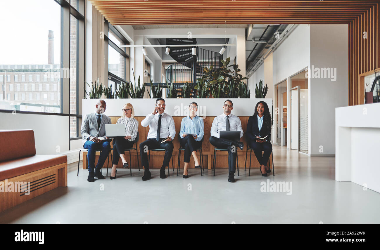 Smiling group de diverses affaires de travailler ensemble tout en étant assis dans une rangée de la réception d'un bureau moderne Banque D'Images