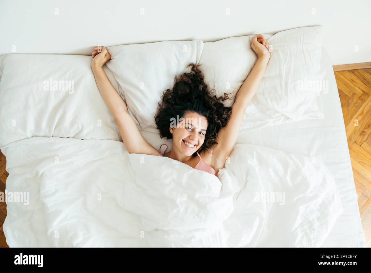 Jolie jeune femme au lit avec draps blancs lumière vive Banque D'Images