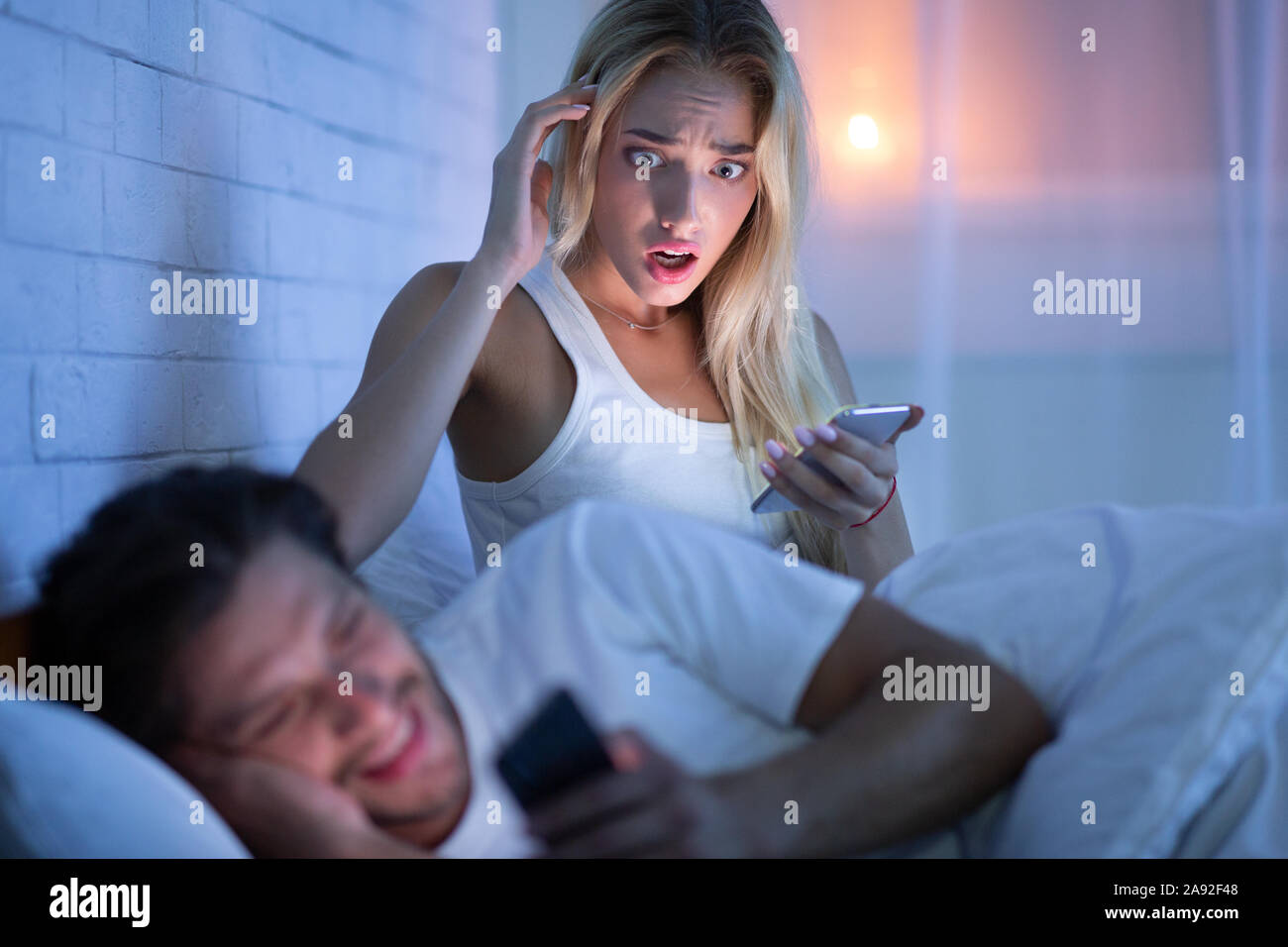 Woman Catching Boyfriend Cheater Chatting On Phone In Bed Piscine Banque D'Images