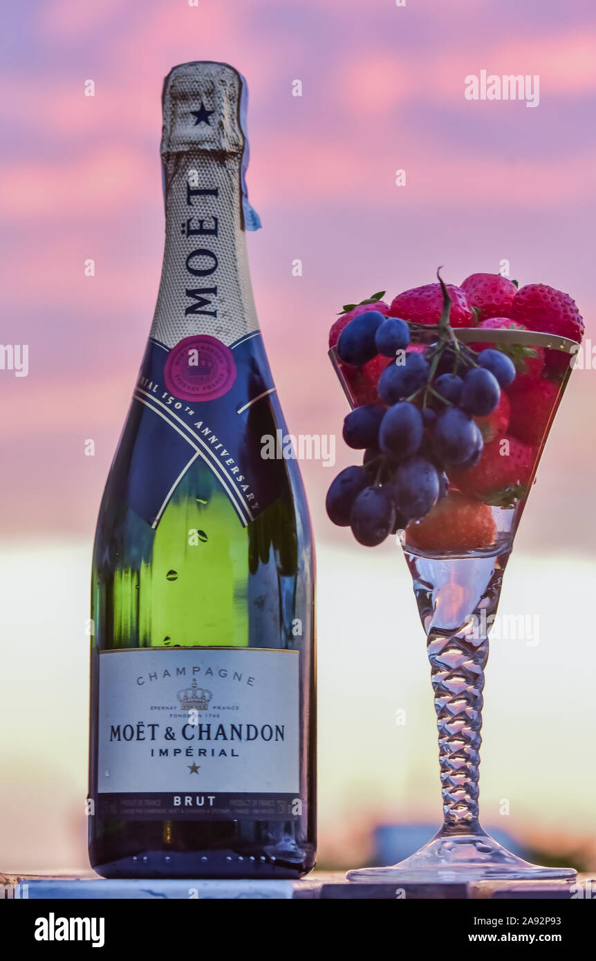 Bouteille de champagne et un verre de champagne avec des raisins et des fruits contre sunset sky Banque D'Images