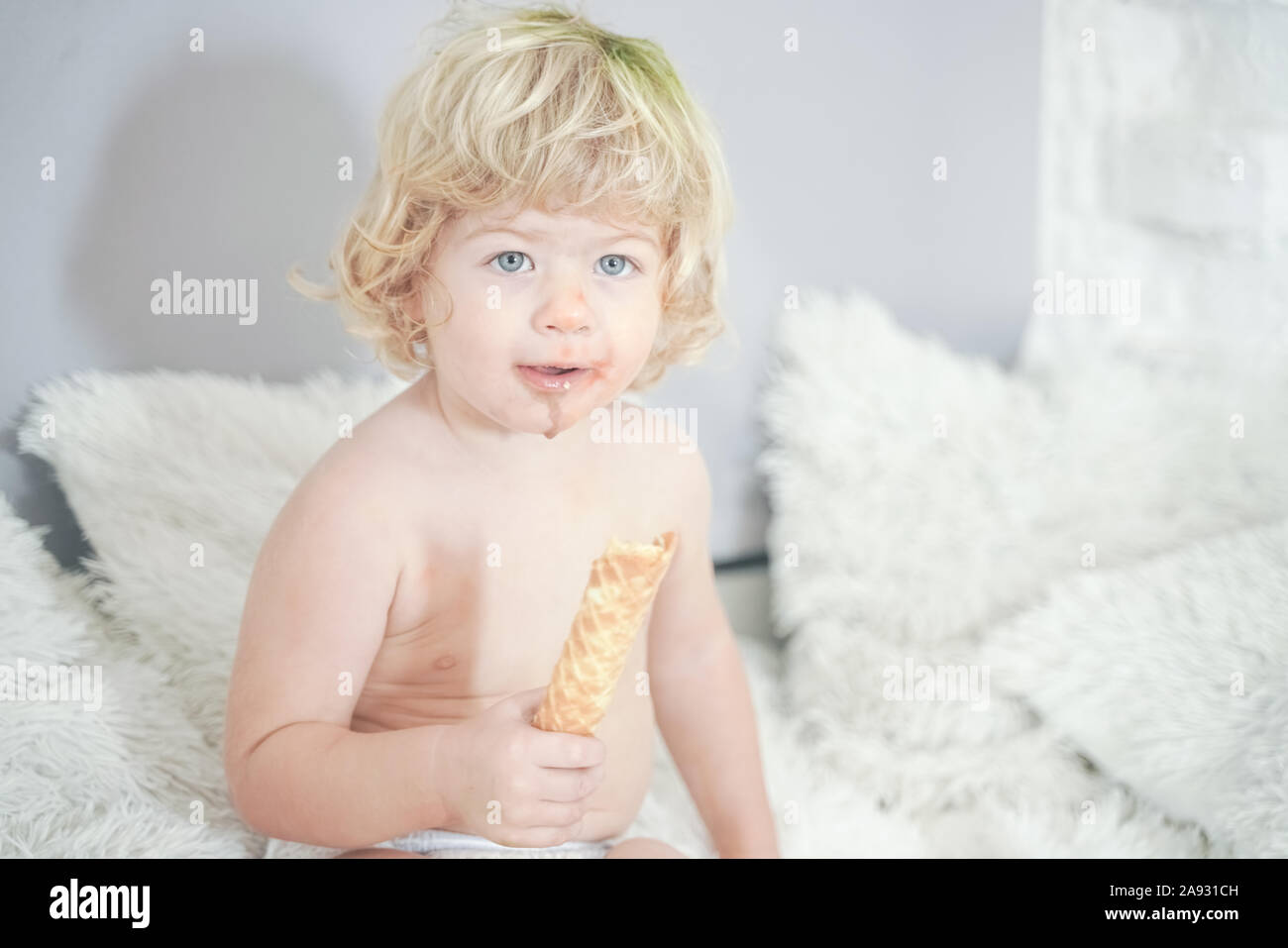 Petit enfant prenant gaufre et le manger avec plaisir et l'amusement sur arrière-plan de la salle blanche. Banque D'Images