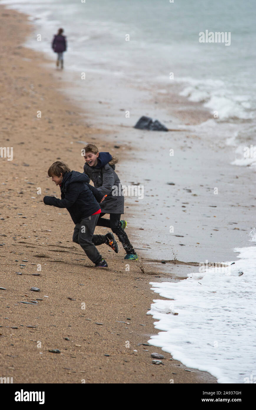 2 garçons courir loin de vagues sur la grève au lieu non identifié, Devon, UK Banque D'Images