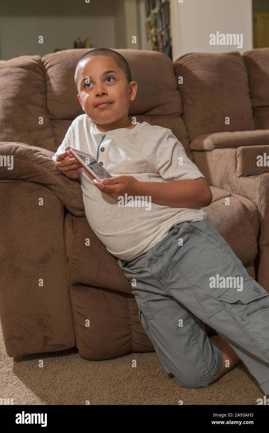 Un garçon hispanique avec l'autisme jouant à des jeux électroniques sur son téléphone dans la salle de séjour Banque D'Images