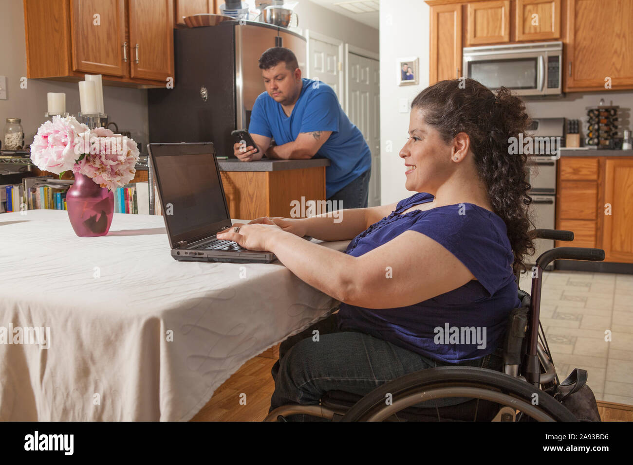 Femme avec Spina Bifida utilisant un ordinateur avec son mari utilisant téléphone à la maison Banque D'Images