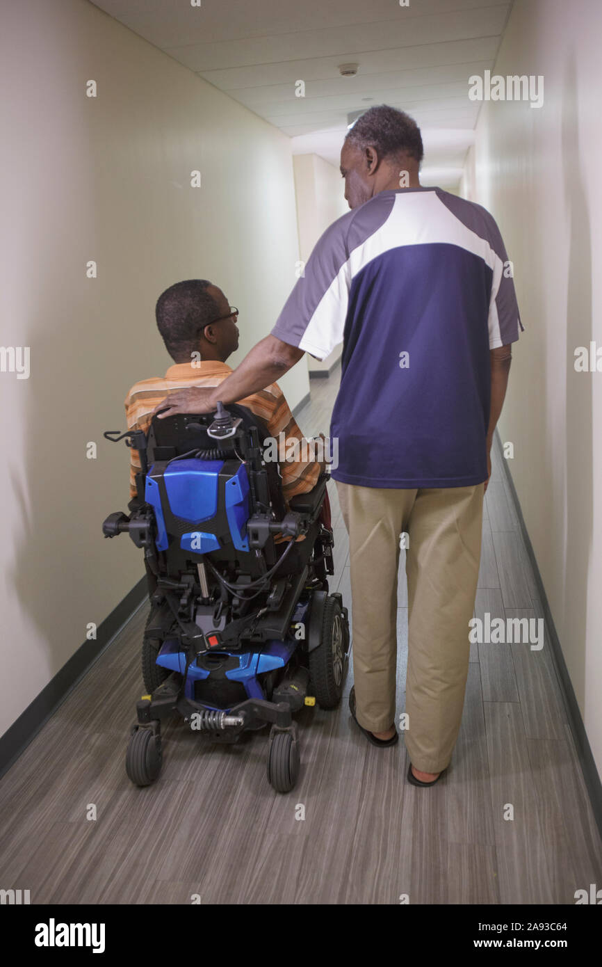Homme avec le syndrome de Guillain-barre dans le couloir de l'appartement sur le pouvoir chaise avec son père Banque D'Images