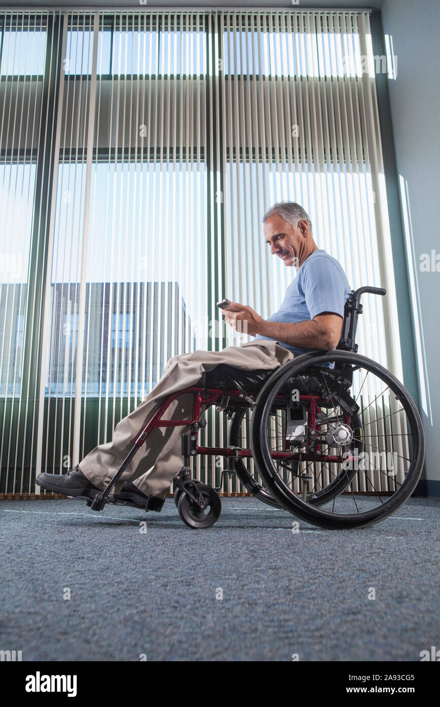 Homme avec une blessure à la moelle épinière sur un fauteuil roulant utilisant le téléphone dedans un couloir de bureau Banque D'Images