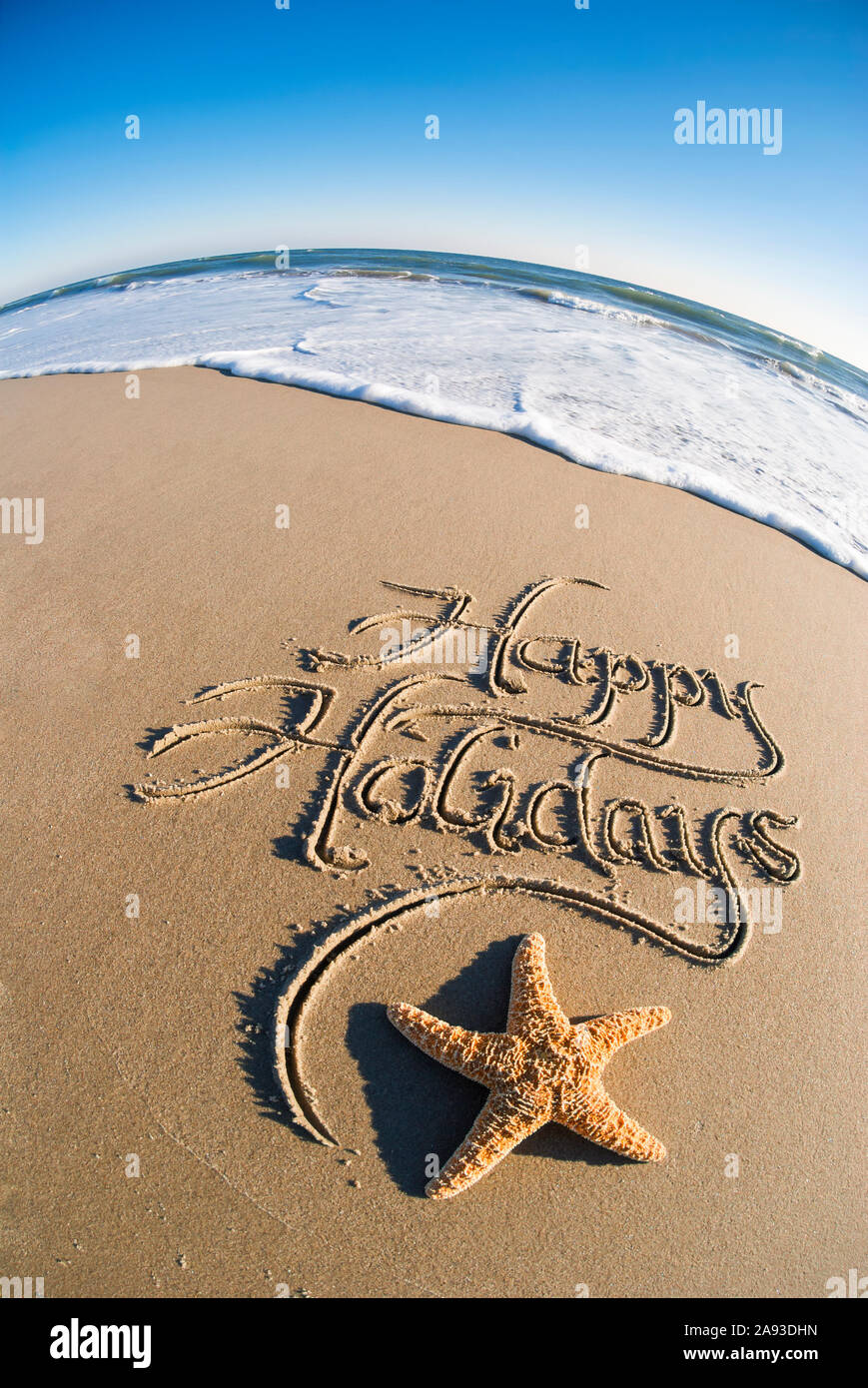 Bonnes vacances message écrit dans le sable lisse avec effet fisheye sur mer et vagues blanc mousseux Banque D'Images