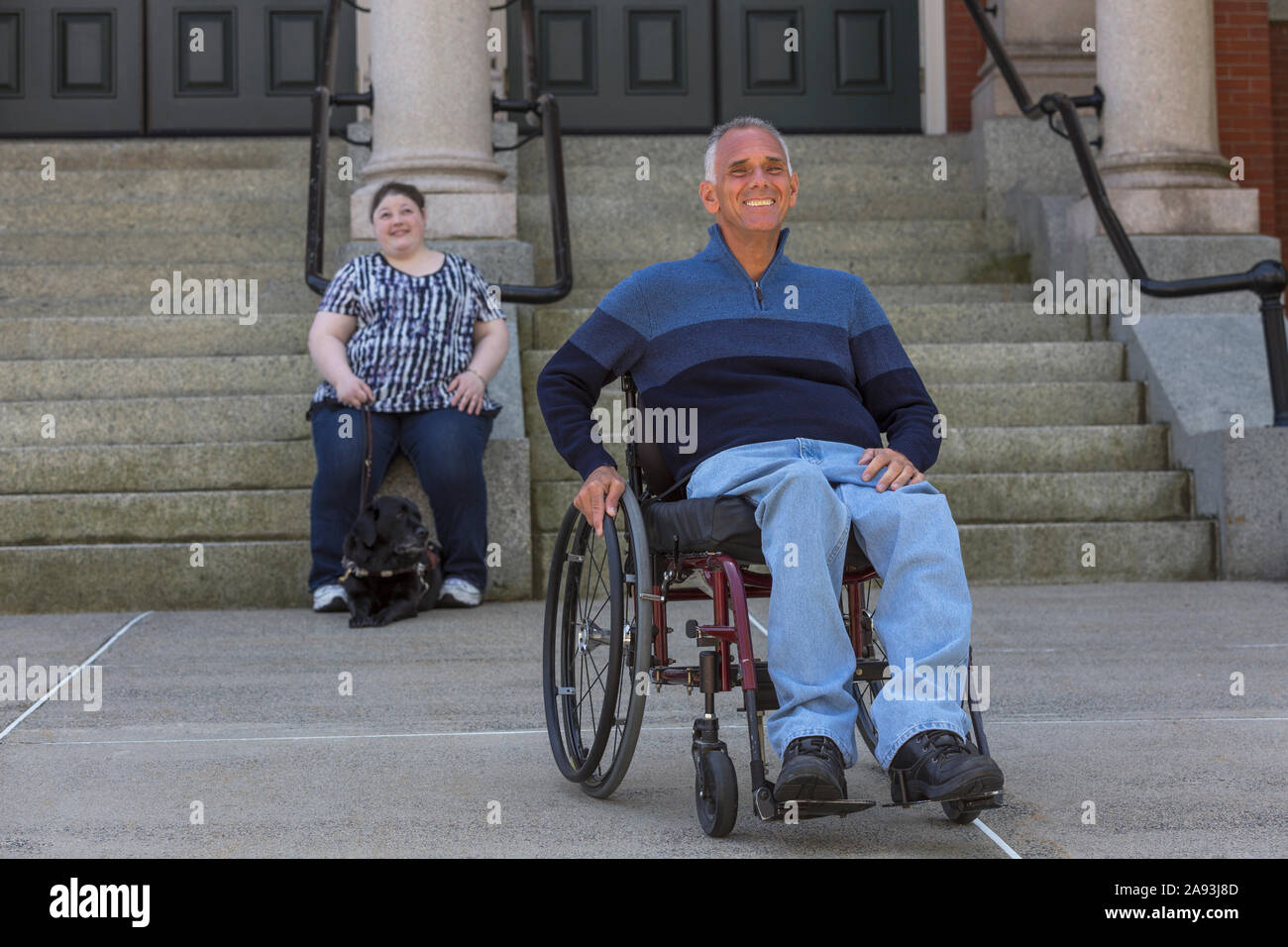Homme blessé à la moelle épinière assis en fauteuil roulant avec son Fille en arrière-plan qui est aveugle Banque D'Images