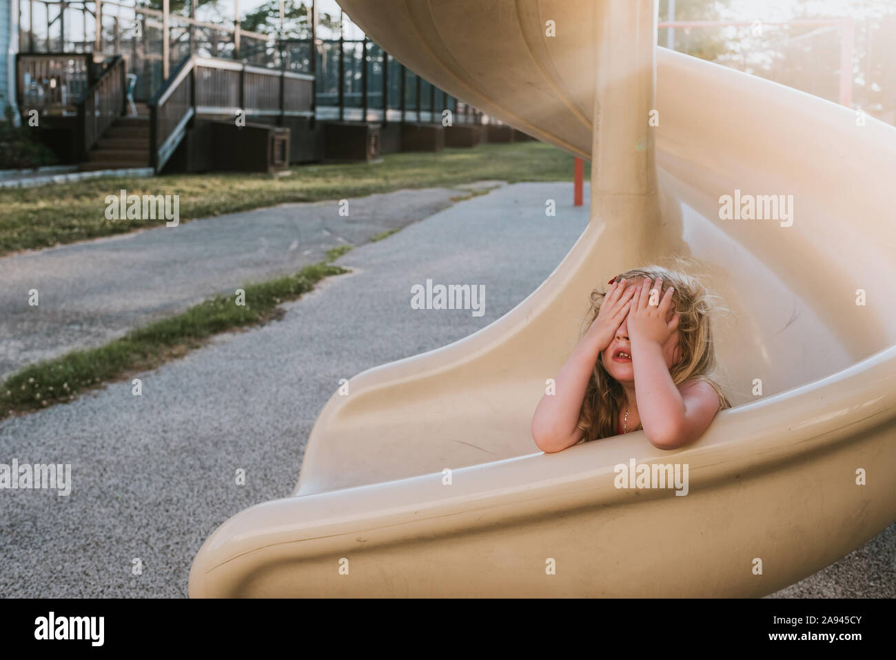 Une petite fille joue à cache-cache sur une diapositive. Banque D'Images