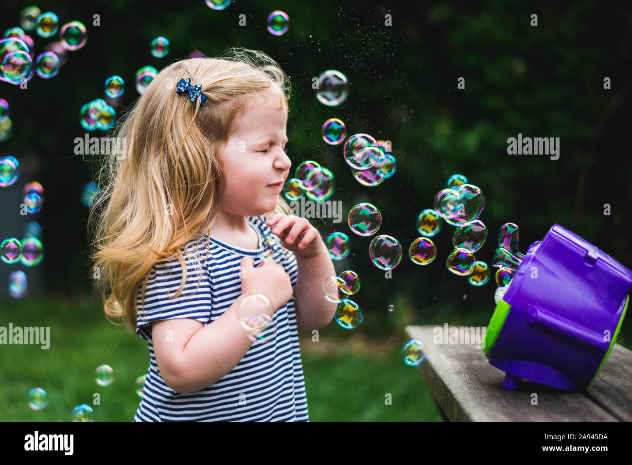 Une petite fille se tient devant une machine à bulles. Banque D'Images