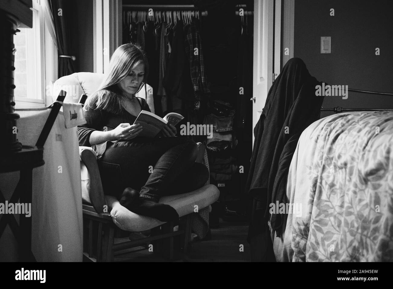 Une femme assise sur une chaise en lisant un livre. Banque D'Images