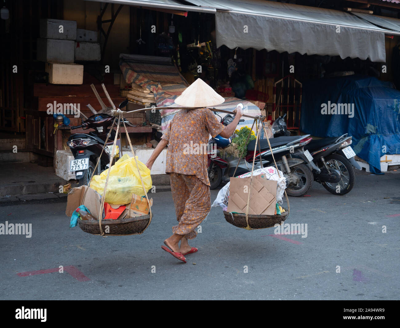 Personnes âgées vietnamienne portant des paniers de carton recyclé et de plastique sur un pôle de transport à Hoi An, Vietnam Banque D'Images