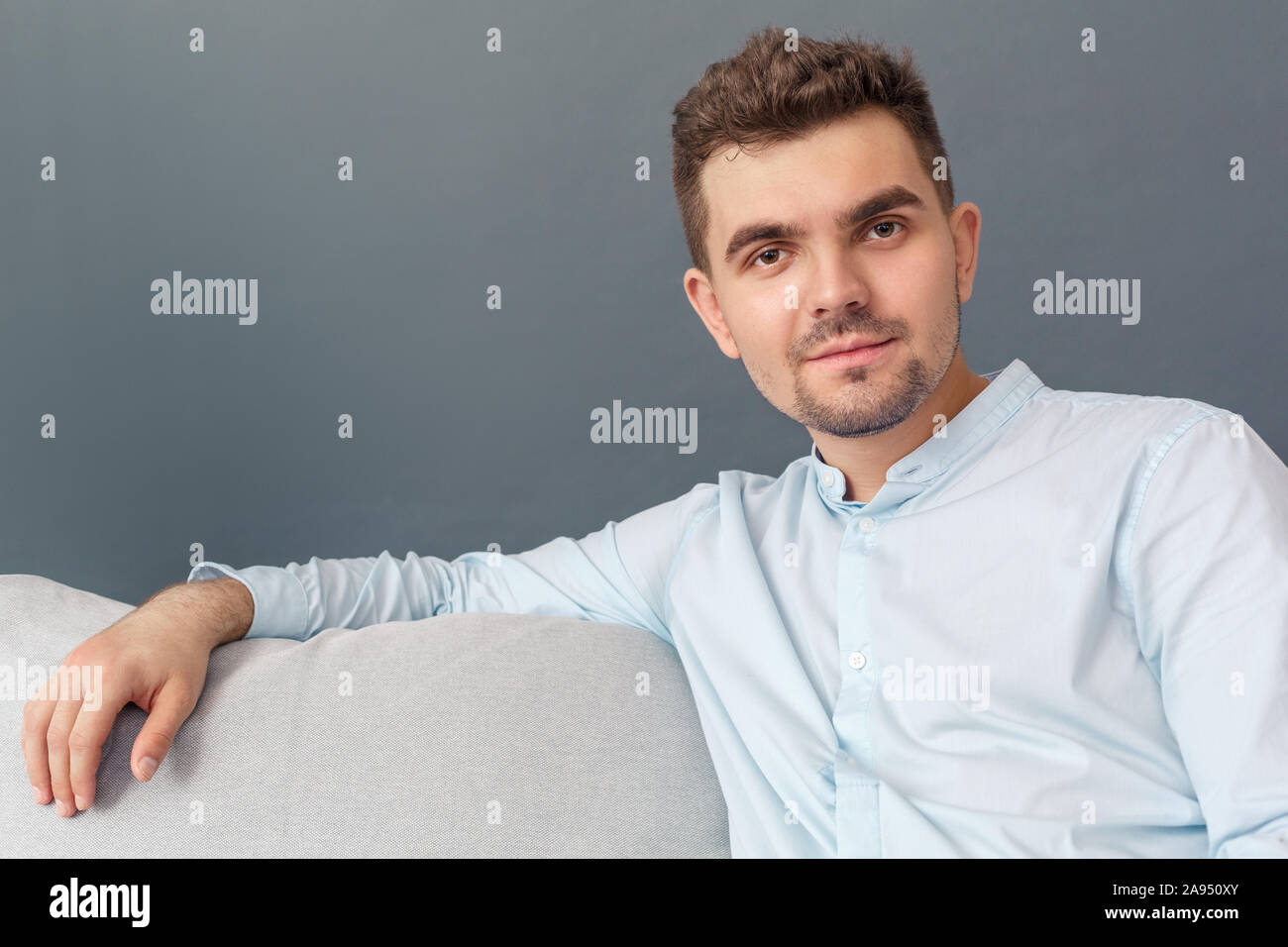 Freestyle. Young man sitting on sofa studio isolé sur calme souriant gris close-up Banque D'Images