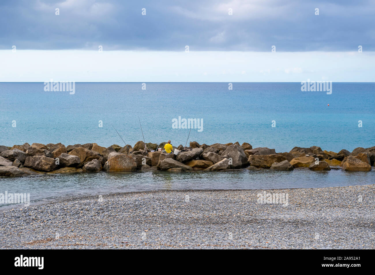 Un homme non identifiables avec des seaux et barres de pêches sur les rochers le long de la côte de Vintimille, Italie, sur la Riviera italienne. Banque D'Images