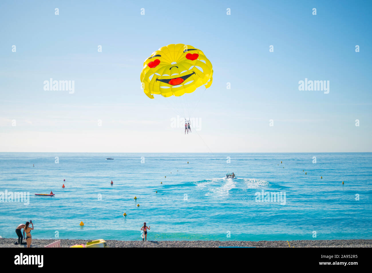 Les touristes en maillots de regarder comme un bateau avec un couple prend le parachute ascensionnel sur la Baie des Anges sur une journée ensoleillée sur la côte d'Azur Banque D'Images