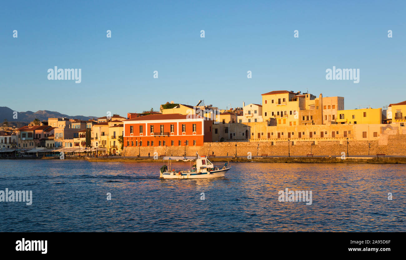 Chania, Crète, Grèce. Vue sur le port vénitien au lever du soleil, bateau de pêche se dirigeant vers la mer. Banque D'Images
