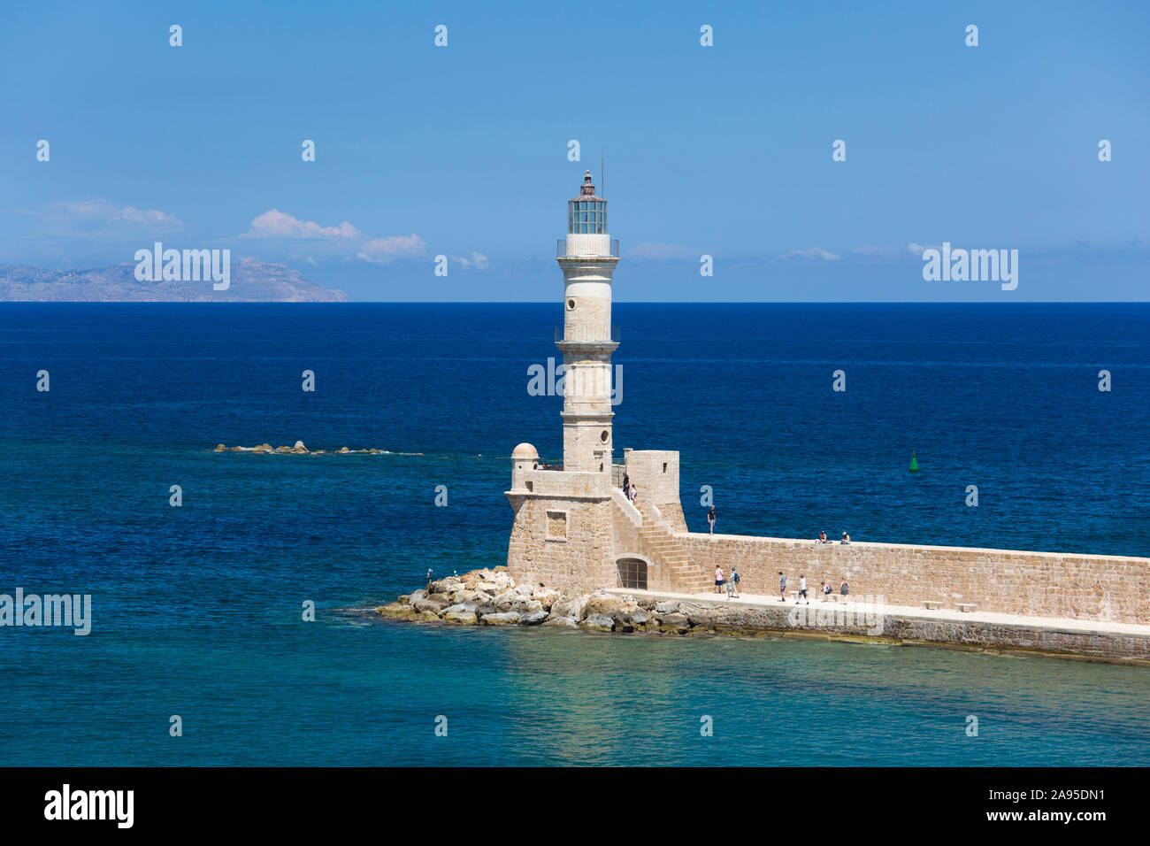 Chania, Crète, Grèce. Vue sur le port vénitien jusqu'au phare historique, touristes visibles sur le mur de la mer. Banque D'Images