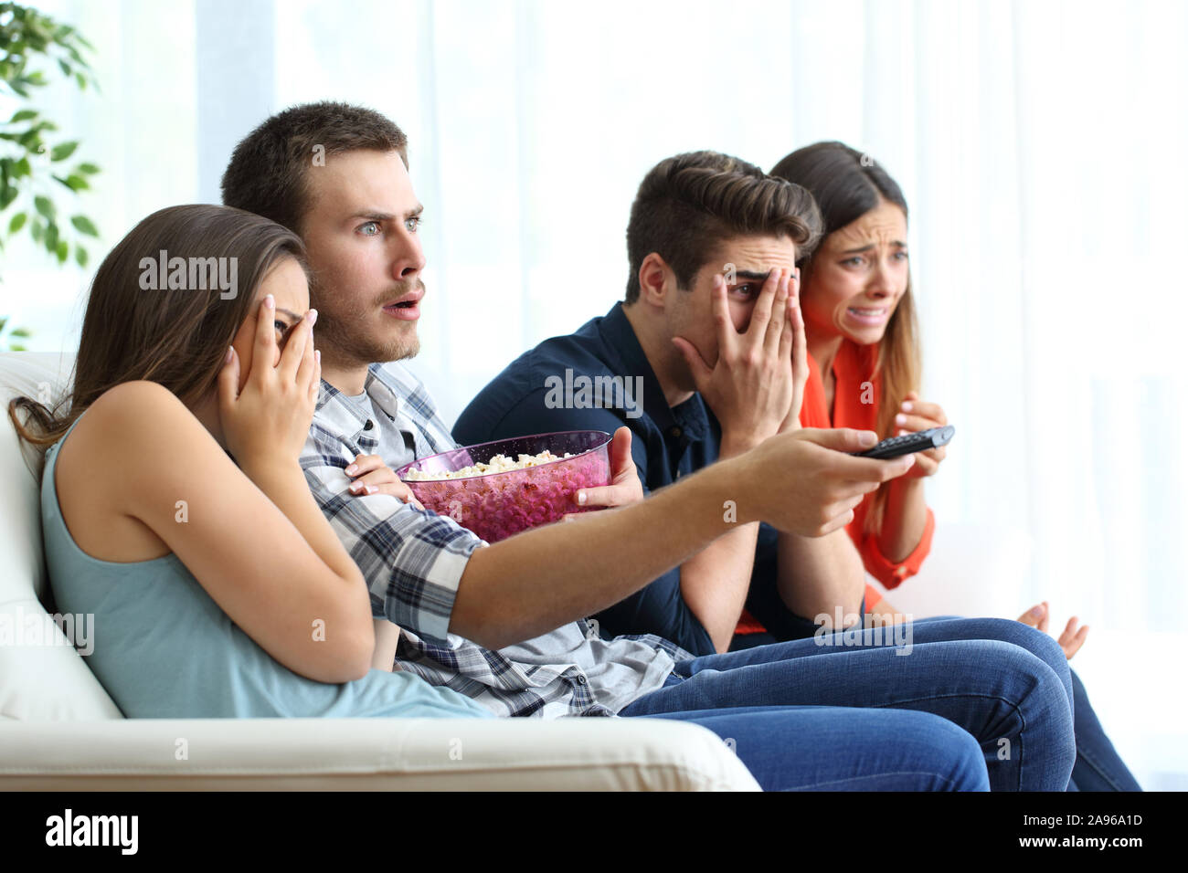 Peur groupe des amis à regarder un film d'horreur à la tv assis sur un canapé dans la salle de séjour à la maison Banque D'Images