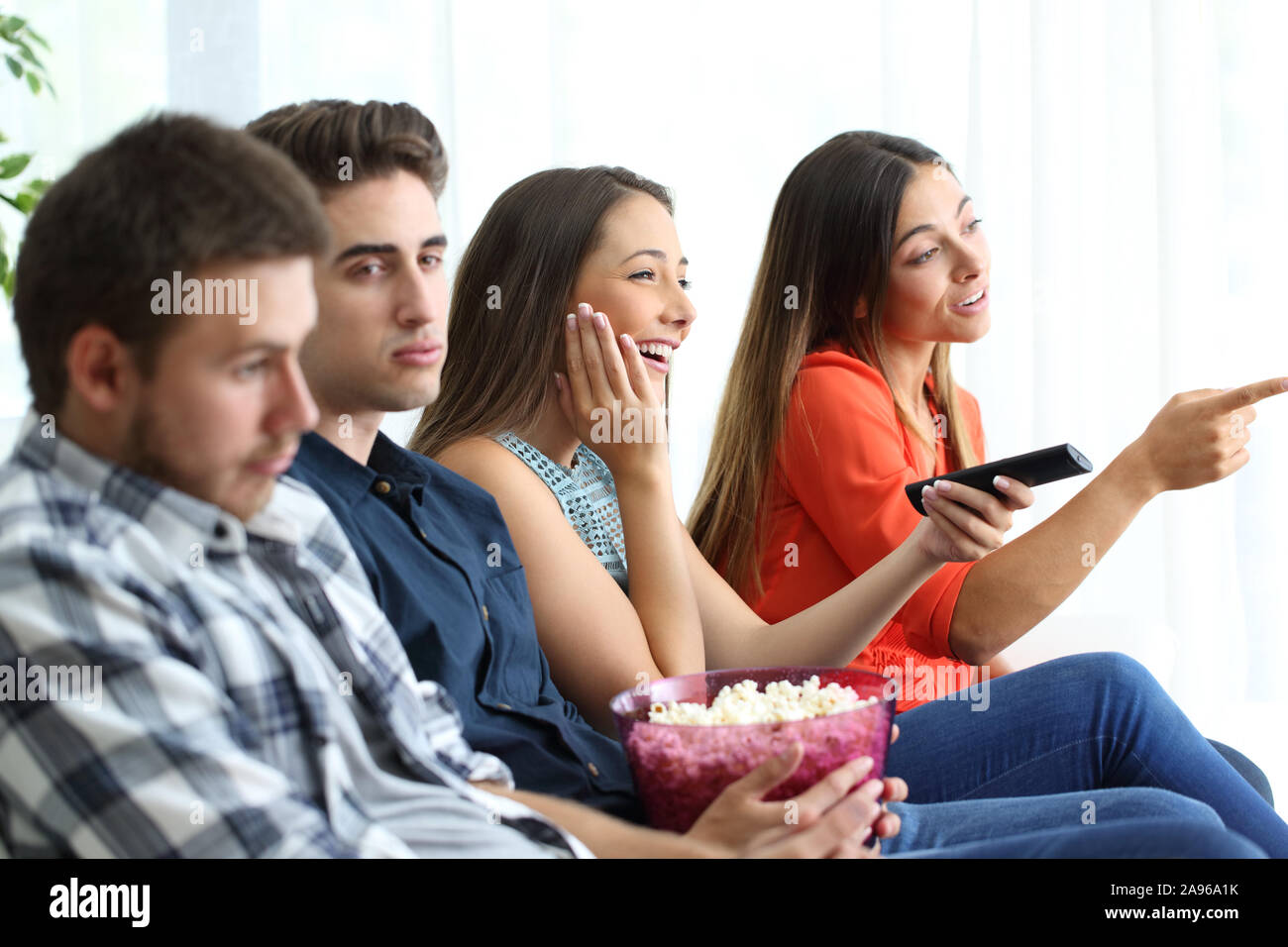Girls Watching film romantique avec leurs petits amis ennuyé assis sur un canapé dans la salle de séjour à la maison Banque D'Images