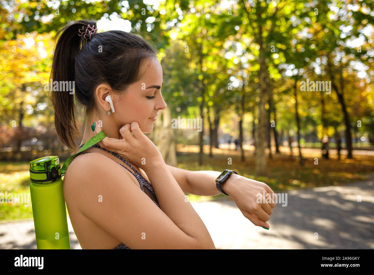 Heureux femme athlétique avec une bouteille d'eau à l'aide de smart watch en parc. copy space Banque D'Images