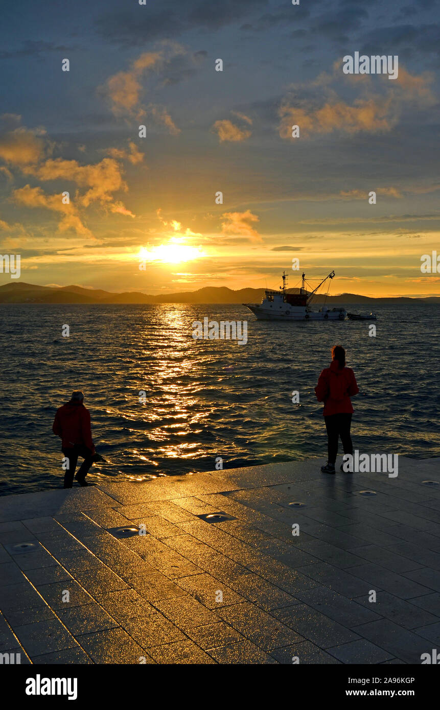 Coucher de soleil incroyable (lever du soleil, l'aube) en mer avec des silhouettes de personnes (couple) et un bateau à Zadar (Croatie) Banque D'Images