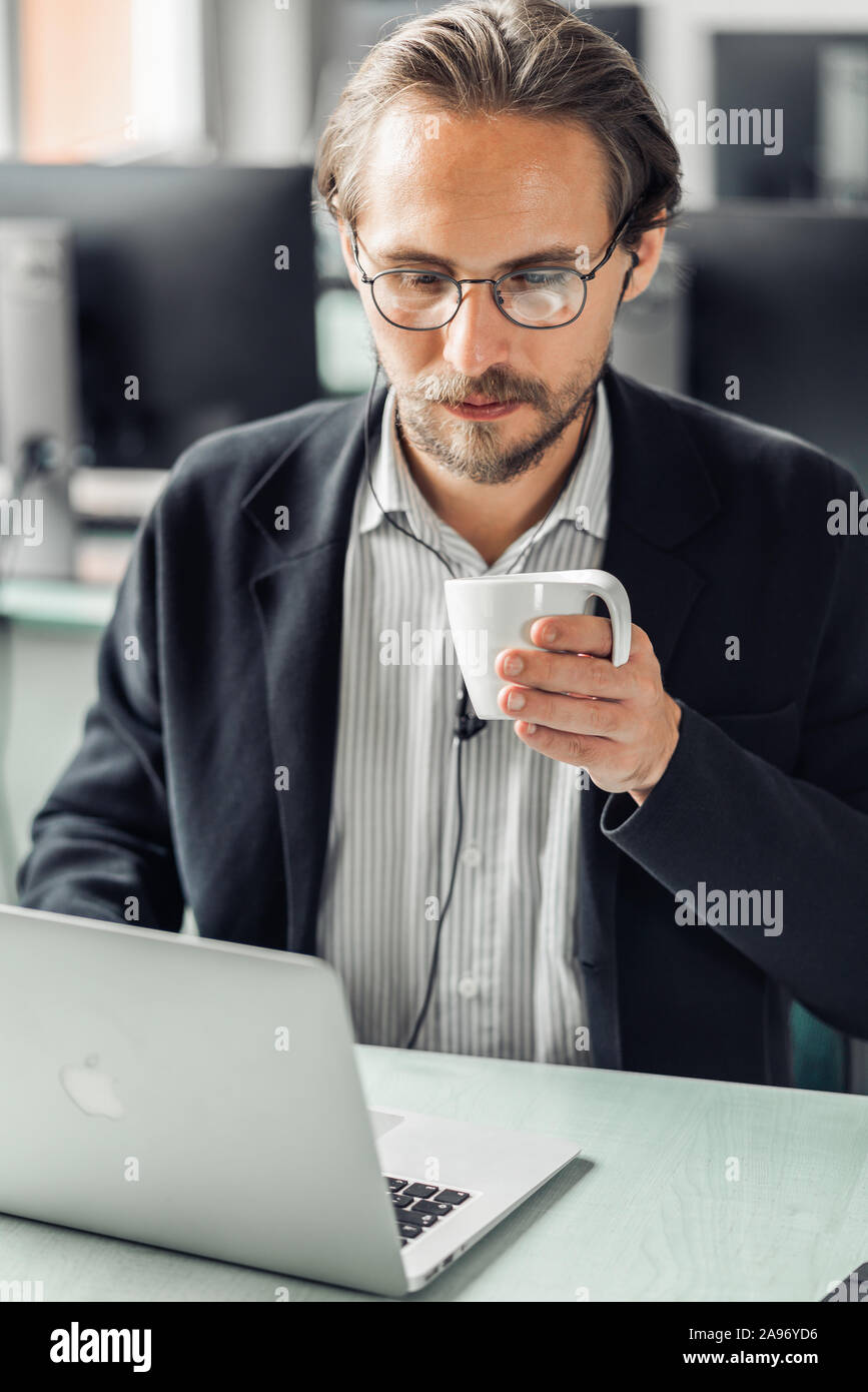Beau jeune homme de boire du café tout en travaillant par le poste informatique. Banque D'Images