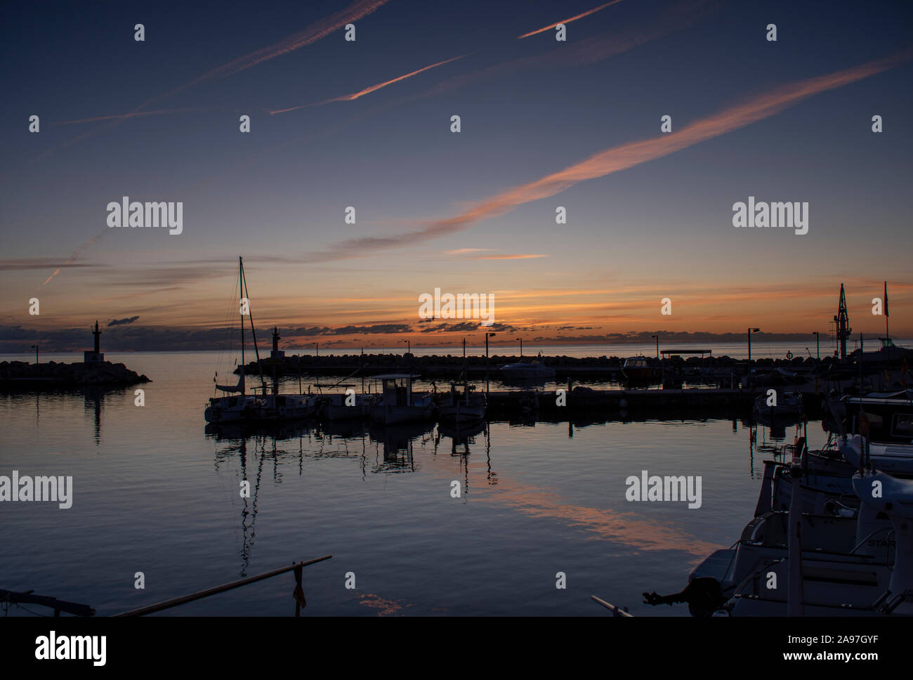 Beau lever de soleil sur le port de plaisance de Cala Bona, Majorque belle couleurs vives et spectaculaires sentiers avion reflétant dans l'eau. Banque D'Images