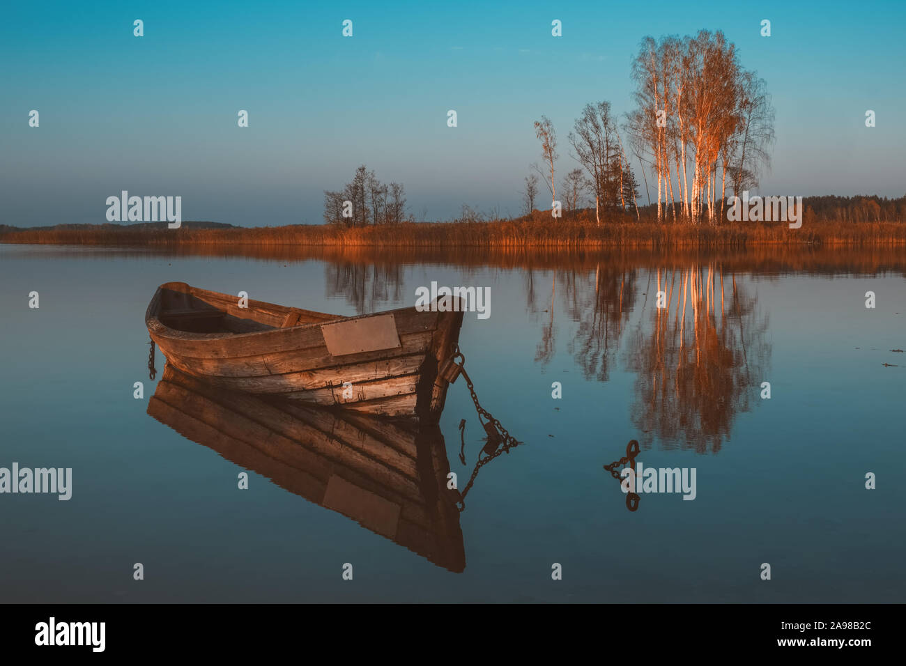 Bateau à rames en bois avec reflet dans un lac au crépuscule de l'eau encore sur paysage d'automne. Banque D'Images