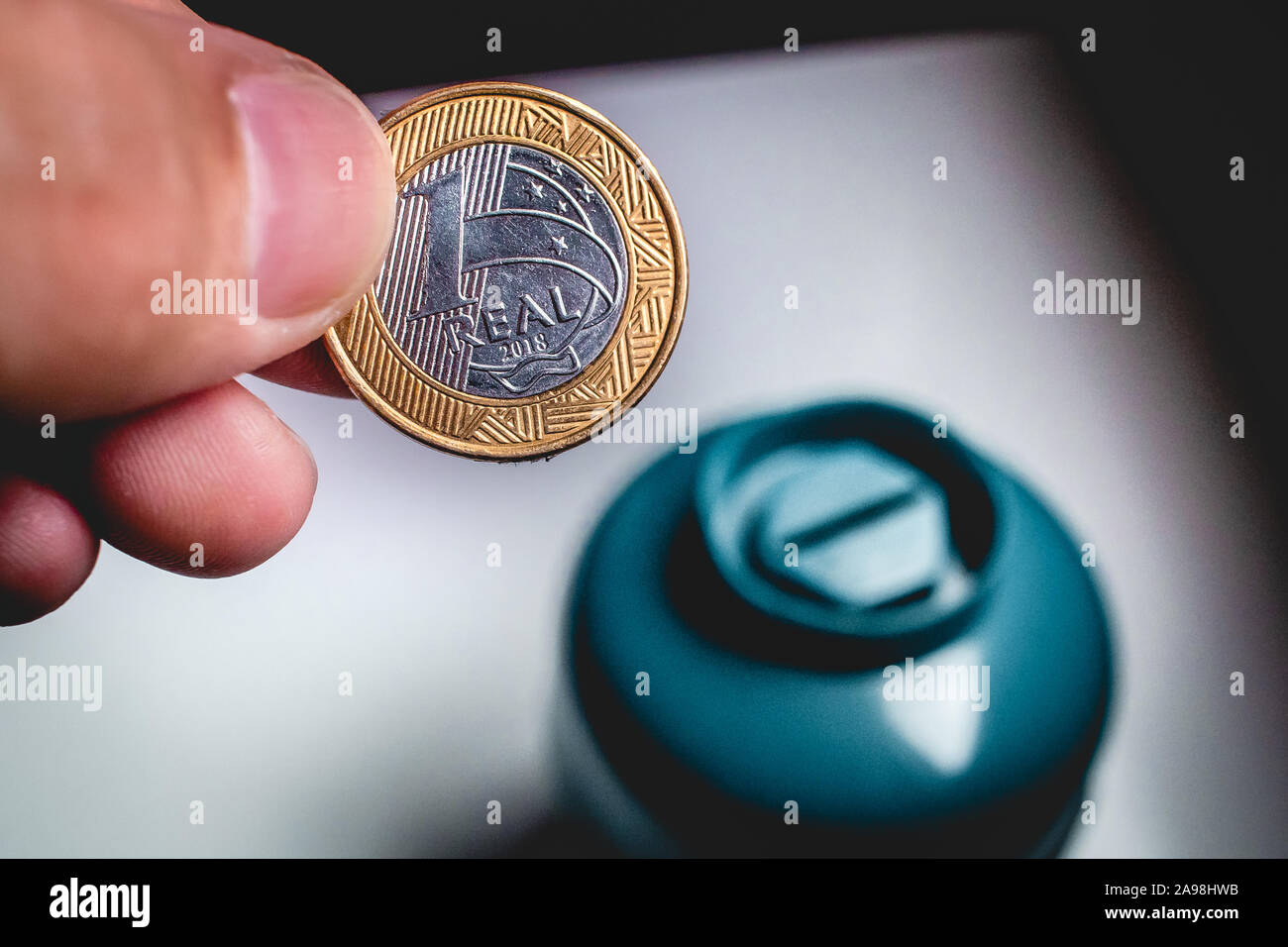 Homme tenant une pièce d'un vrai (monnaie brésilienne) à mettre dans un coin de la banque. Banque D'Images