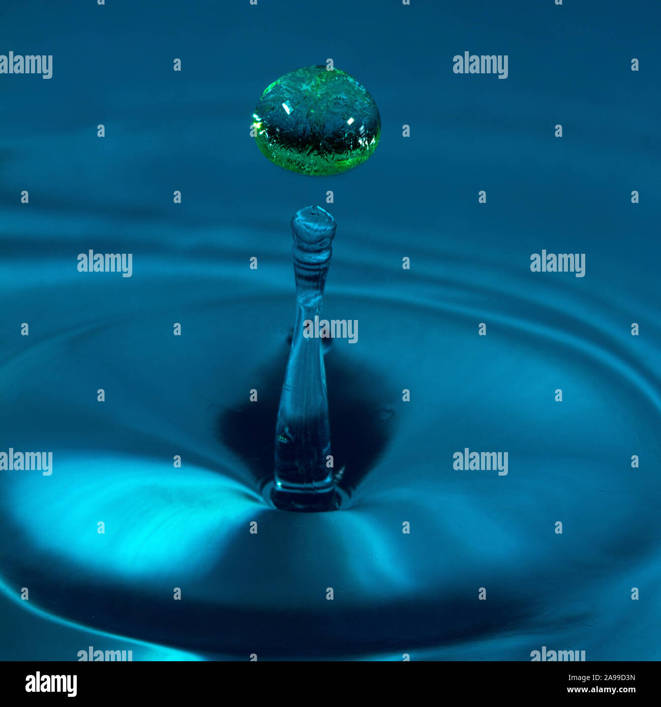 Les gouttes d'eau colorée publié à l'heure précise d'être capturée par l'appareil. La bulle verte prend la couleur du fond du plat. Banque D'Images