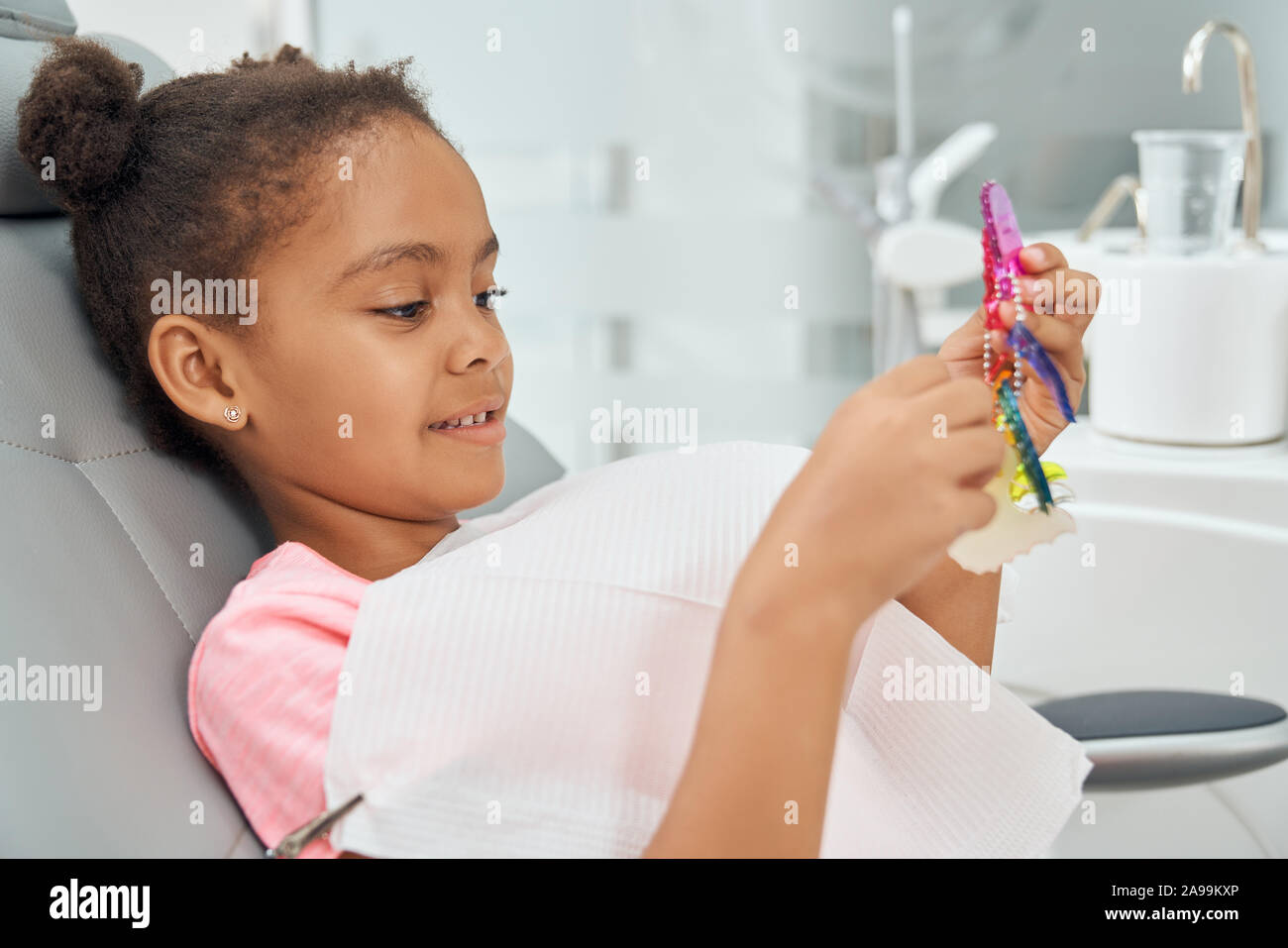 Jeune fille visiter cabinet dentaire. En Afrique, un enfant assis dans fauteuil dentaire avec blanc bib. Beau, mignon, et considérant la tenue des patients gras colorolful accolades pour l'alignement des dents. Banque D'Images