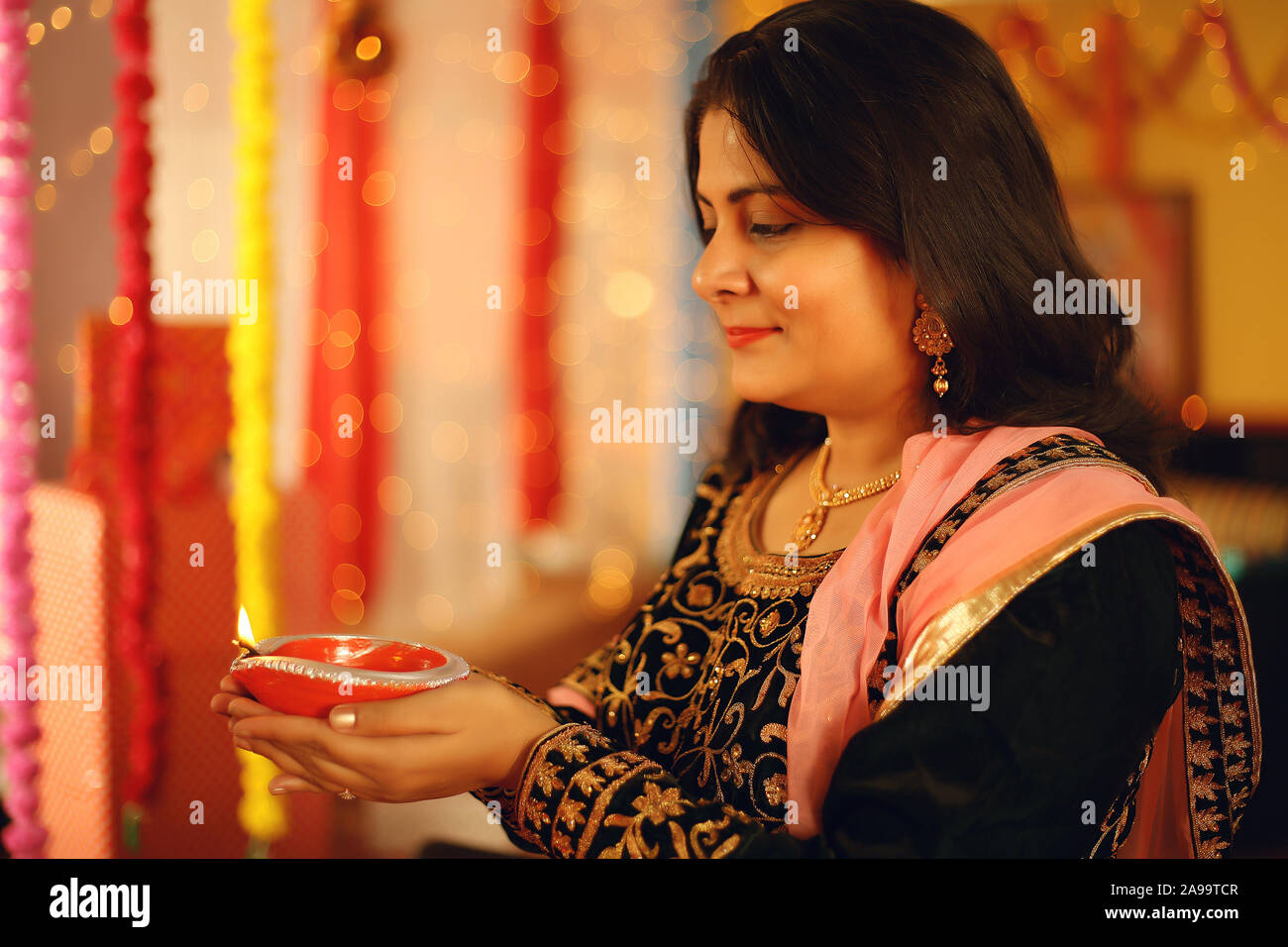 Une belle jeune femme indienne en sari traditionnel dress holding une lampe à huile légère ou Diya dans l'arrière-plan décoratif à l'occasion de Diwali Banque D'Images