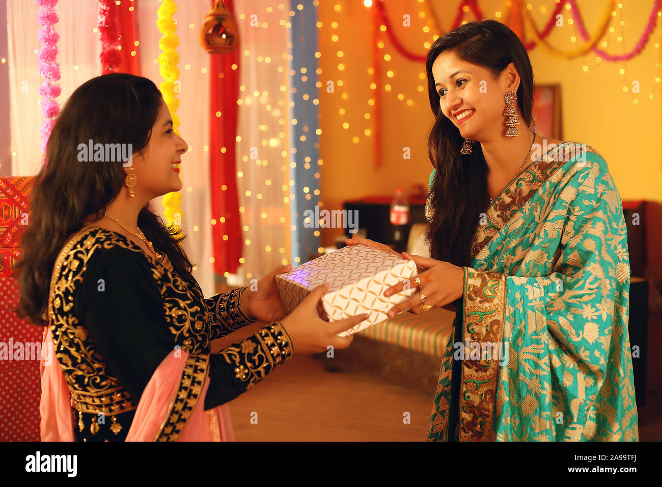 Jolie jeune femme indienne portant des vêtements ethniques traditionnels donner un cadeau à une femme, plus de flou d'arrière-plan de fête. Banque D'Images
