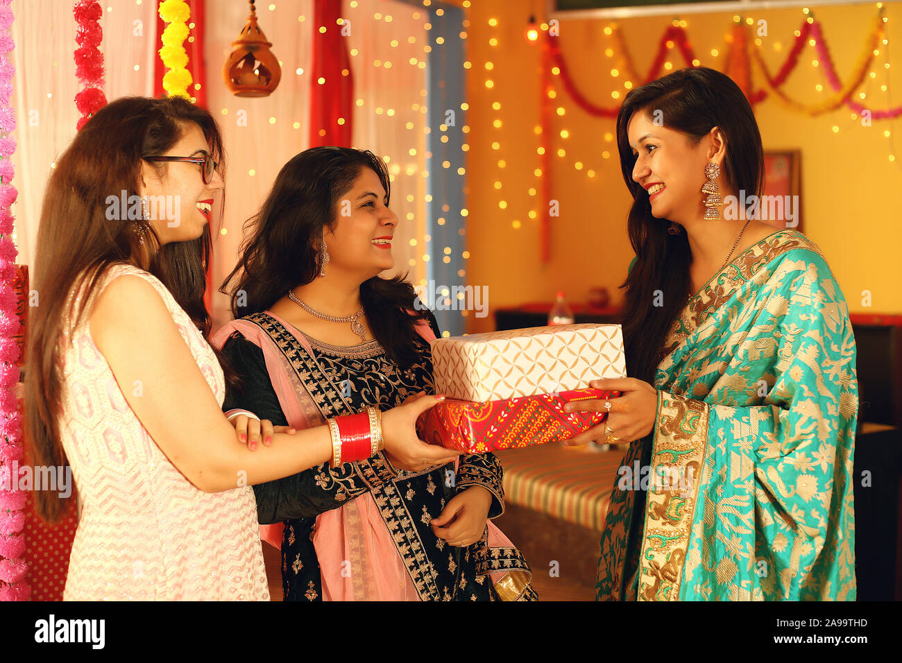 Jolies jeunes femmes indiennes portant des vêtements ethniques traditionnels cadeau donner à une femme, plus de flou d'arrière-plan de fête. Banque D'Images