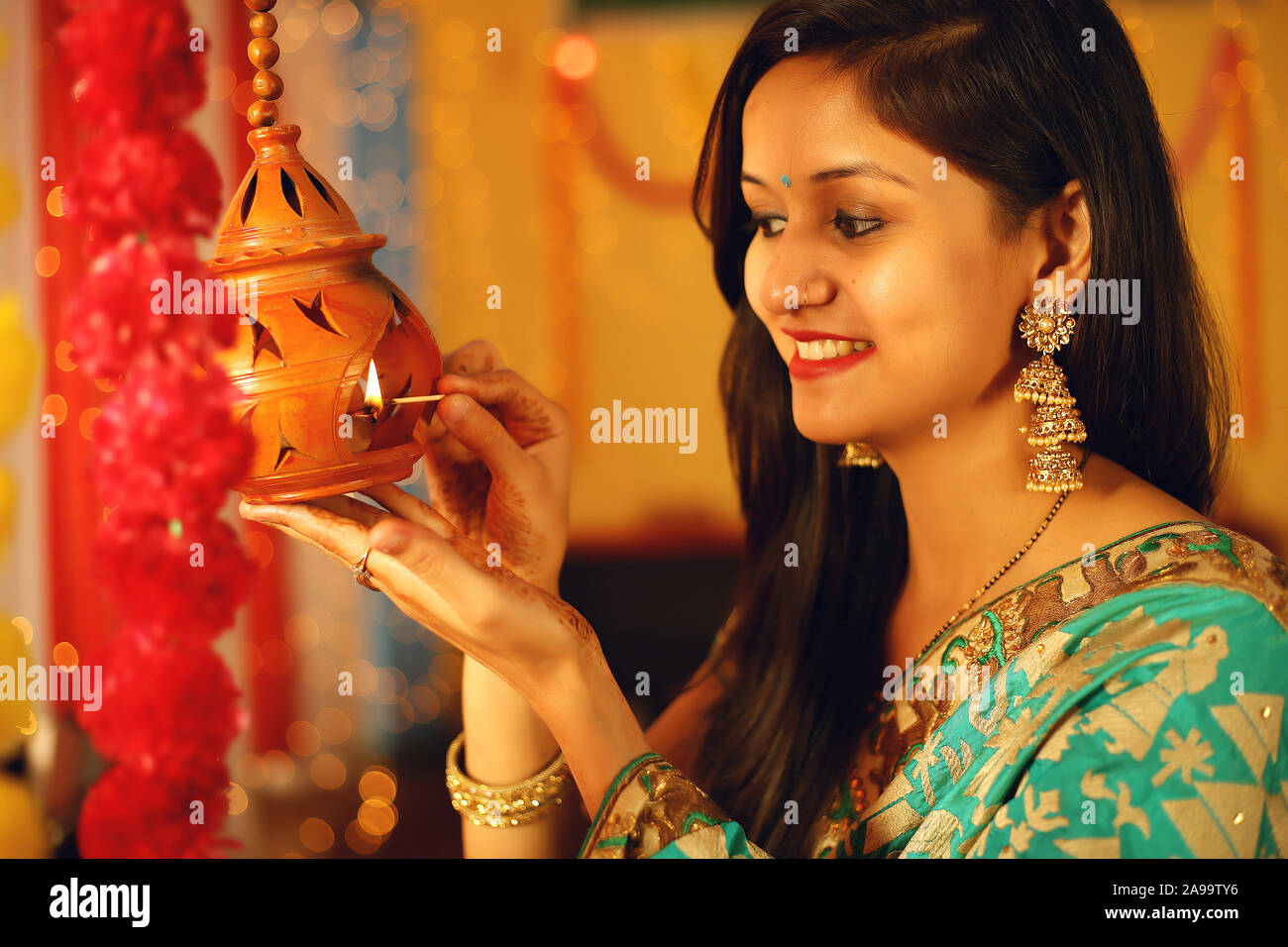 Une belle jeune femme indienne en sari traditionnel dress holding une lampe à huile légère ou Diya au sein de l'arrière-plan décoratif à l'occasion de Diwali. Banque D'Images