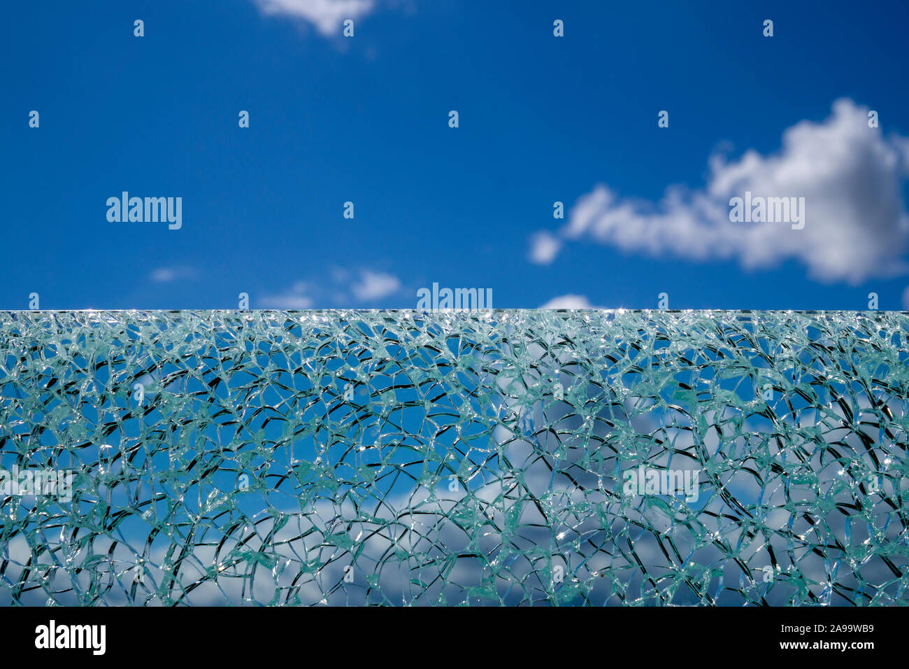 Surface en verre craquelé sur fond de ciel bleu à partir de l'angle faible, avec des nuages blancs flous en arrière-plan Banque D'Images
