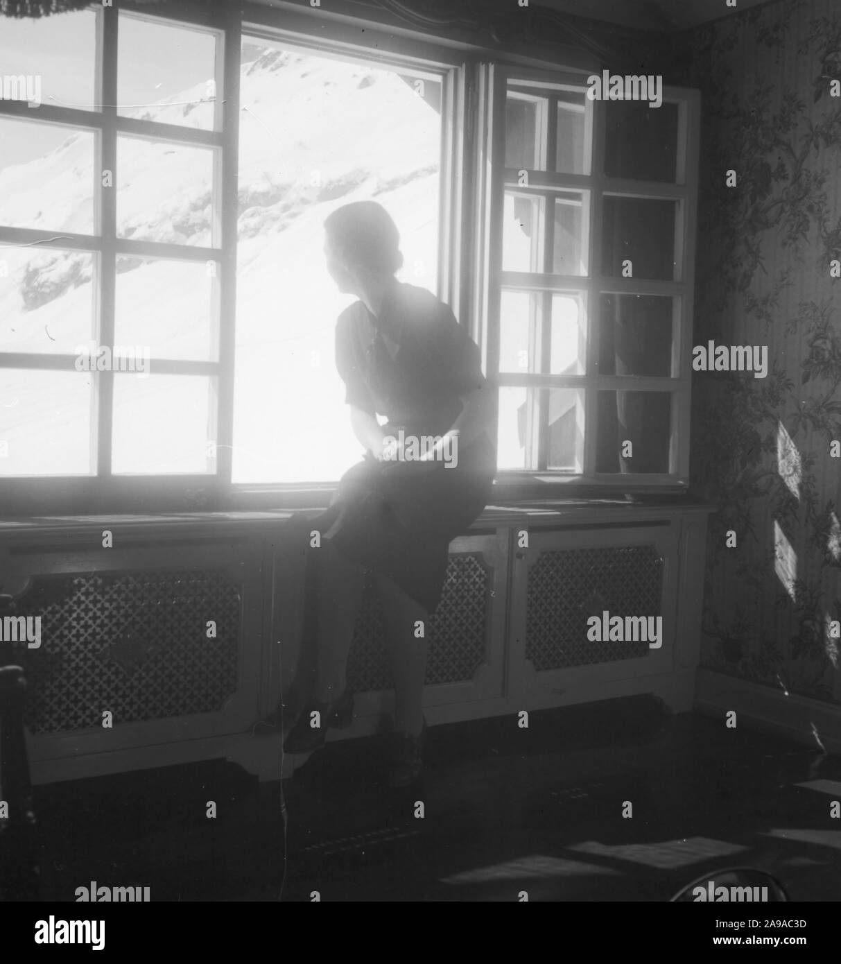 Une jeune femme à la fenêtre d'un hôtel avec vue sur Zuerserhof au plan de l'hôtel dans la région d'Arlberg, Autriche 1930. Banque D'Images