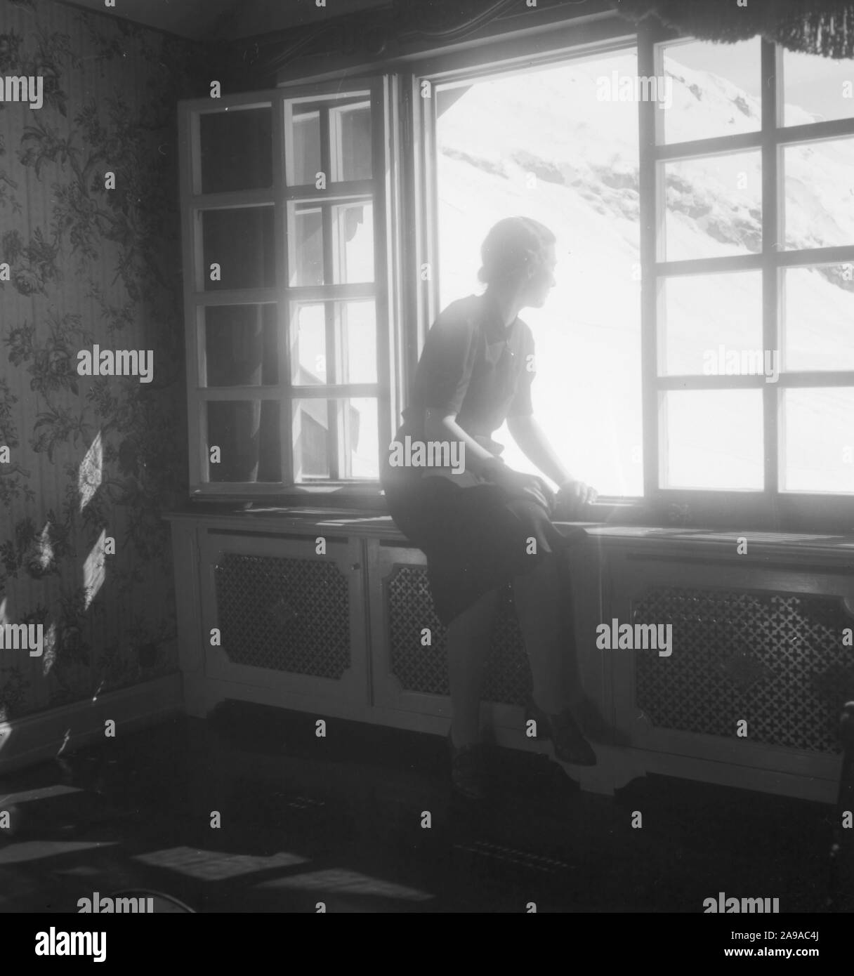 Une jeune femme à la fenêtre d'un hôtel avec vue sur Zuerserhof au plan de l'hôtel dans la région d'Arlberg, Autriche 1930. Banque D'Images