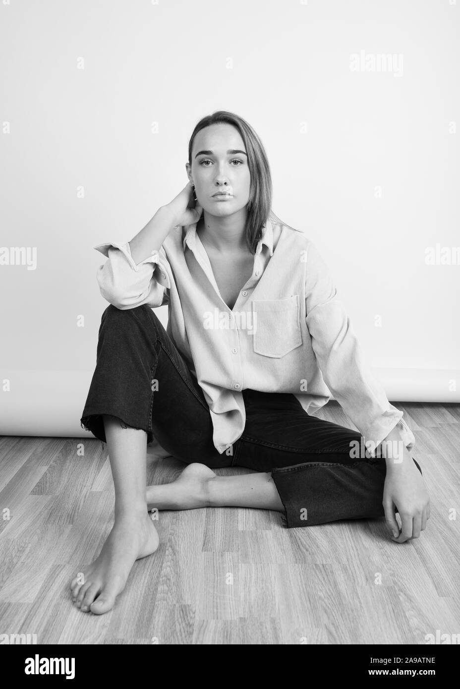 Portrait noir et blanc d'une brunette femme assise pieds nus sur le plancher de bois Banque D'Images