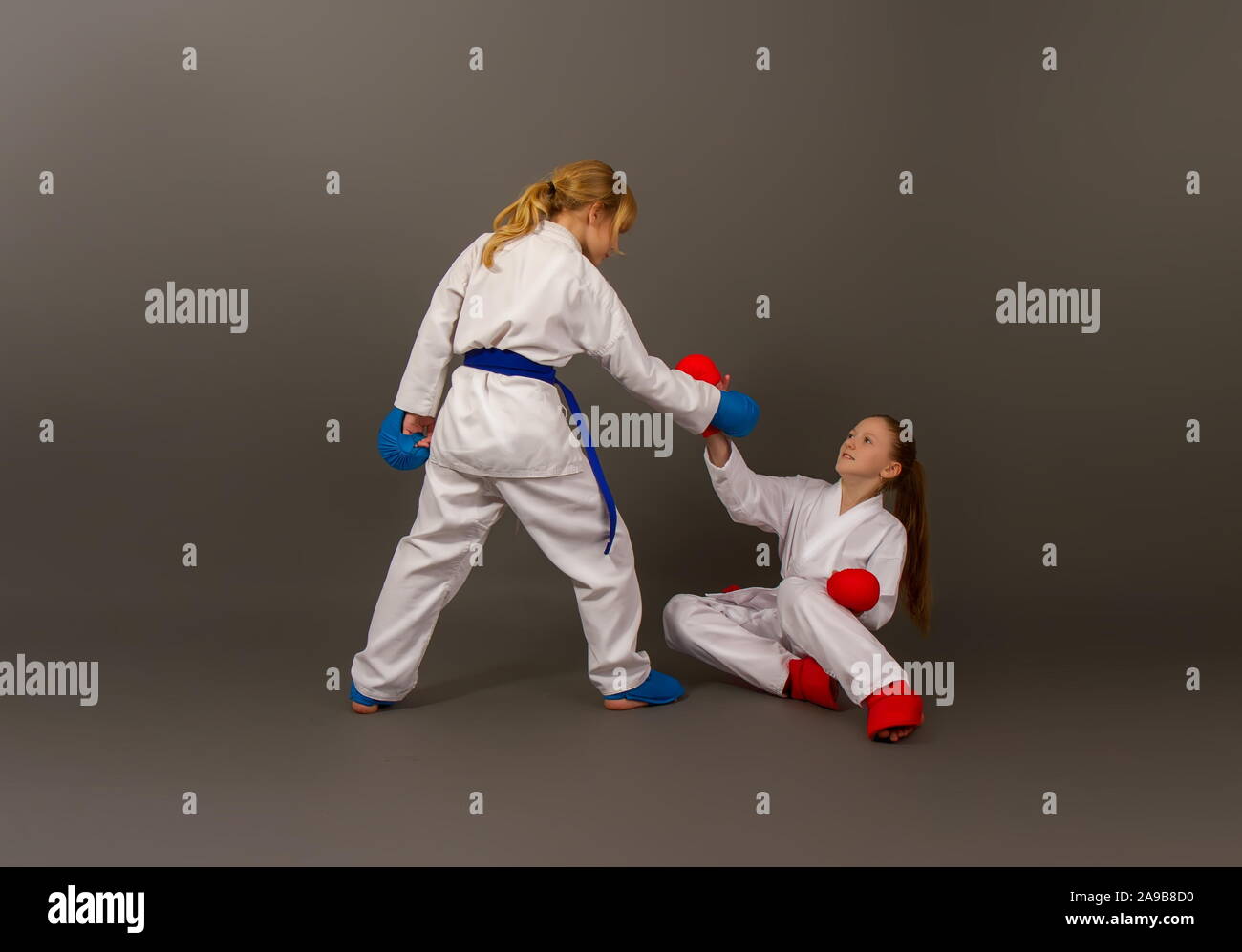 Deux petites filles dans un kimono de karaté et de sports de plein d'équipement de protection rouge et bleu couleurs aider un adversaire qui est tombé au combat à monter. Banque D'Images