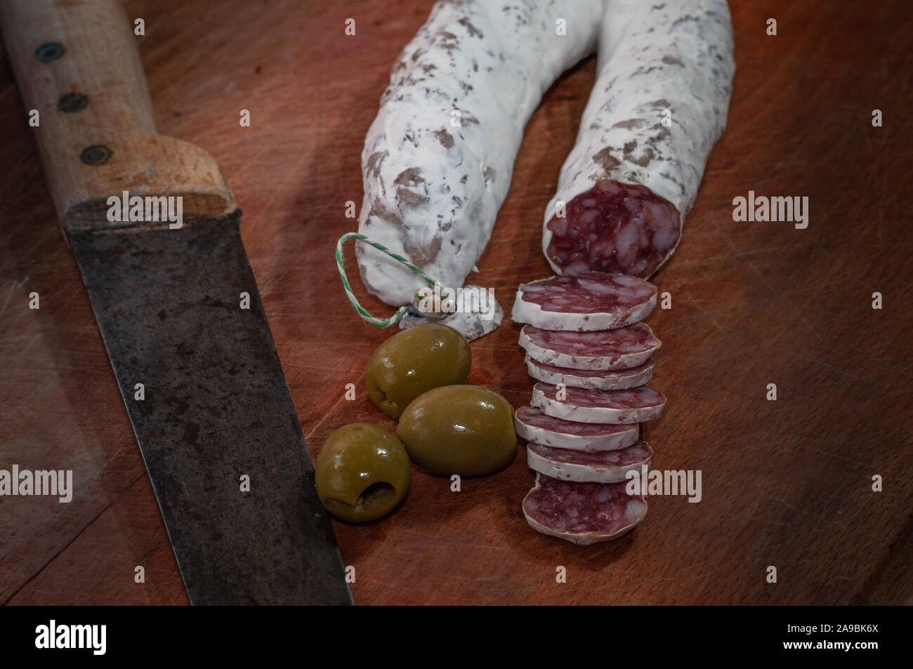 Saucisson sec français ou saucisson. sur une planche à découper avec couteau et olives. Banque D'Images