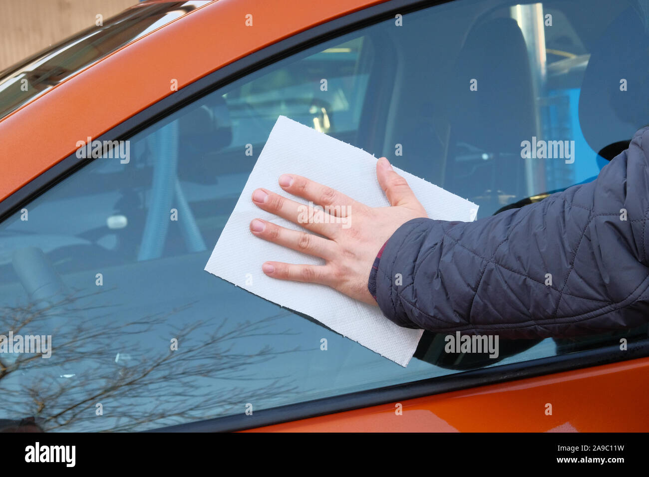 Après l'homme de verre lingettes lavage fenêtre avec une serviette en papier blanc. La main des hommes de corps de voiture et close up. Lavage de voiture à voiture Orange. Banque D'Images